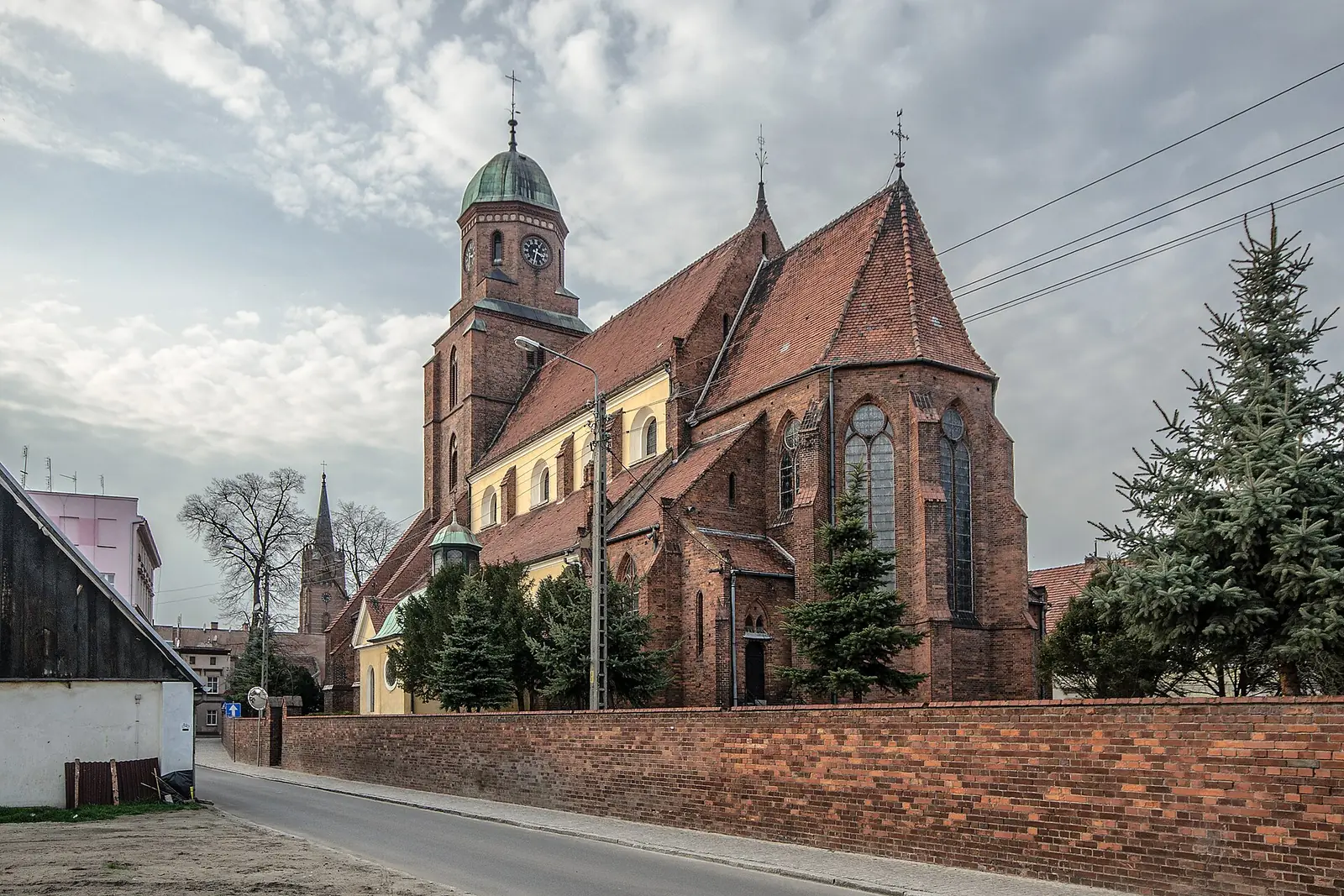 Bryła trójnawowej bazyliki Trójcy Świętej z boku, za ceglanym murem ogrodzenia