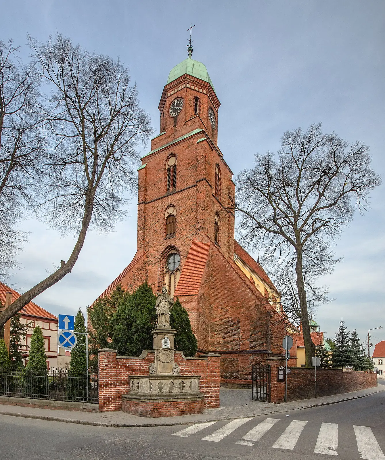 Ceglana wieża kościoła Trójcy Świętej w Żmigrodzie z miedzianym hełmem, widok od skrzyżowania